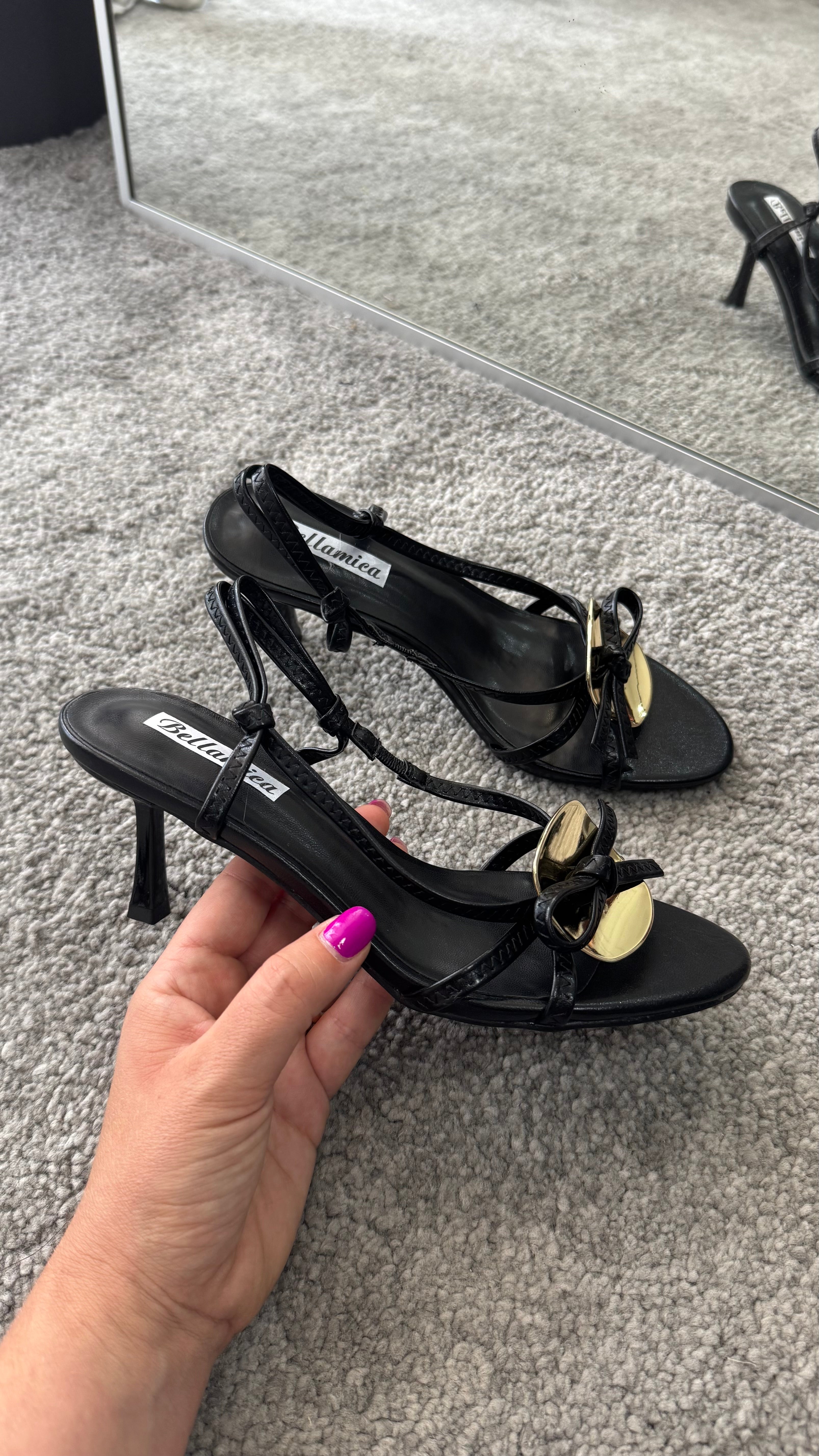 Elegant Sandalo Penelope black heels with 5cm heel, gold accessory, and bow detail, perfect for stylish occasions.