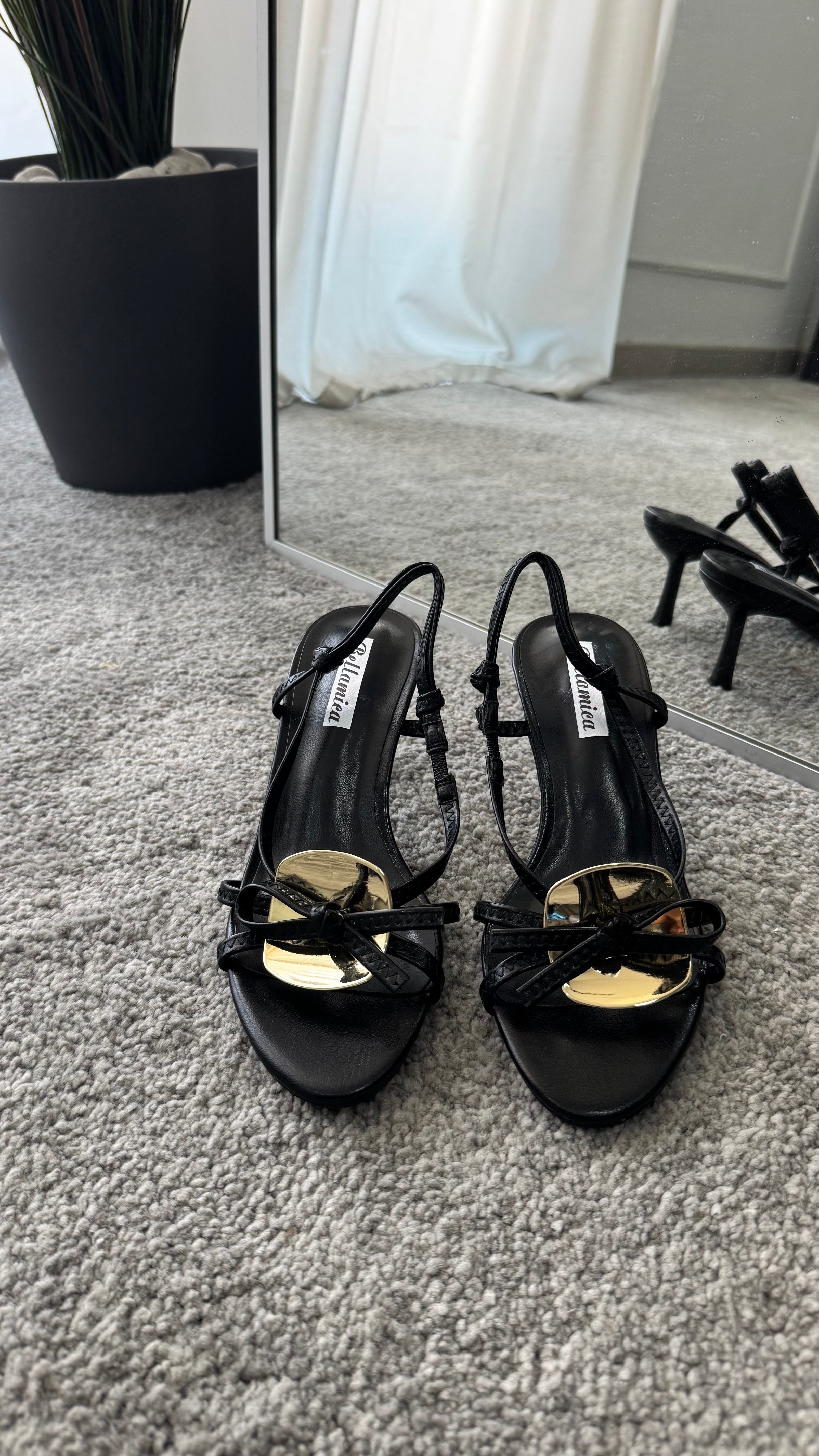 Elegant black heeled sandals with a 5cm heel, featuring a gold accessory and bow detail.